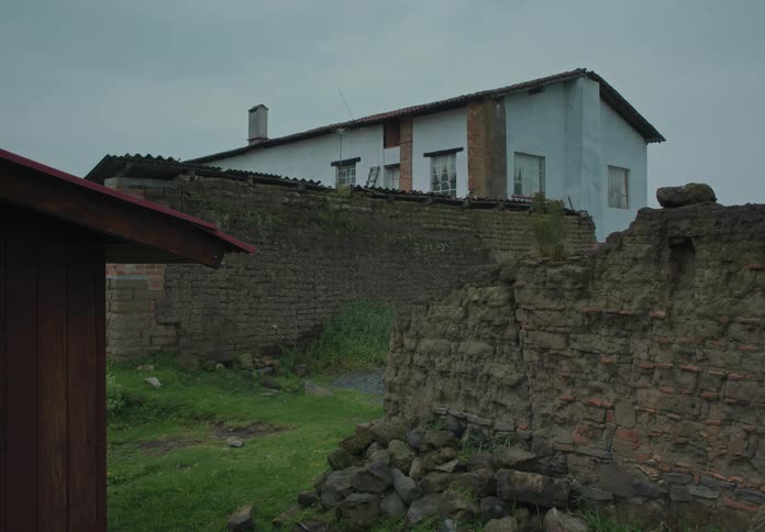 A two story residential building stands beyond some brink walls in need of repair
