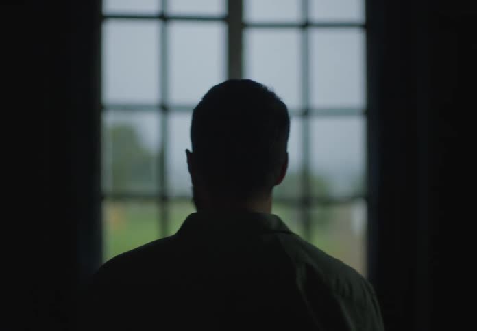 Silhouette of the back of a man standing in front of a window inside a house