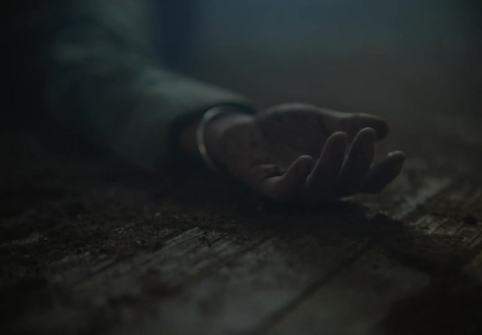 Close up of the hand of a person laying on the floor of a room filled with smoke