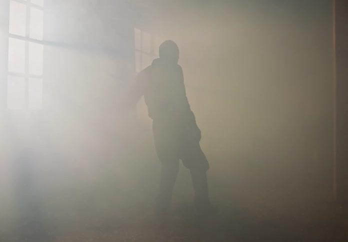 A man in a room filled with smoke stumbles and falls to the ground
