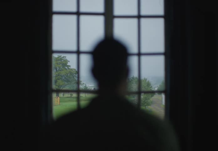 Man walking towards a window indoors and looking out