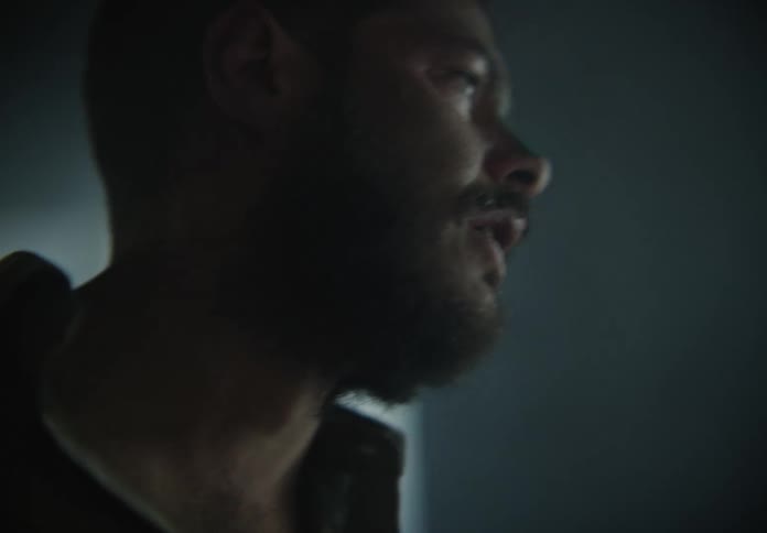 A bearded man appears disoriented and can be seen speaking while in a room