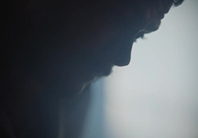 A man in a smoke filled rooms puts his hand up to his head and stumbles