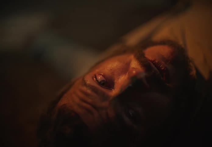 A man lies in the dark and turns his head and looks up when a light is turned on