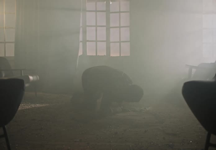 A man in a room filled with smoke lies on the floor and struggles to get up