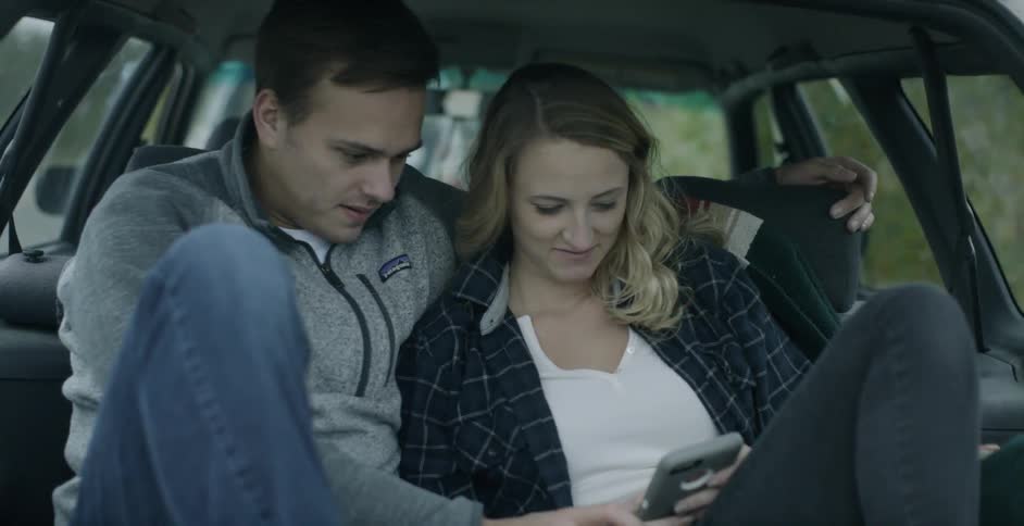 A man and woman in a car looks a phone and talk