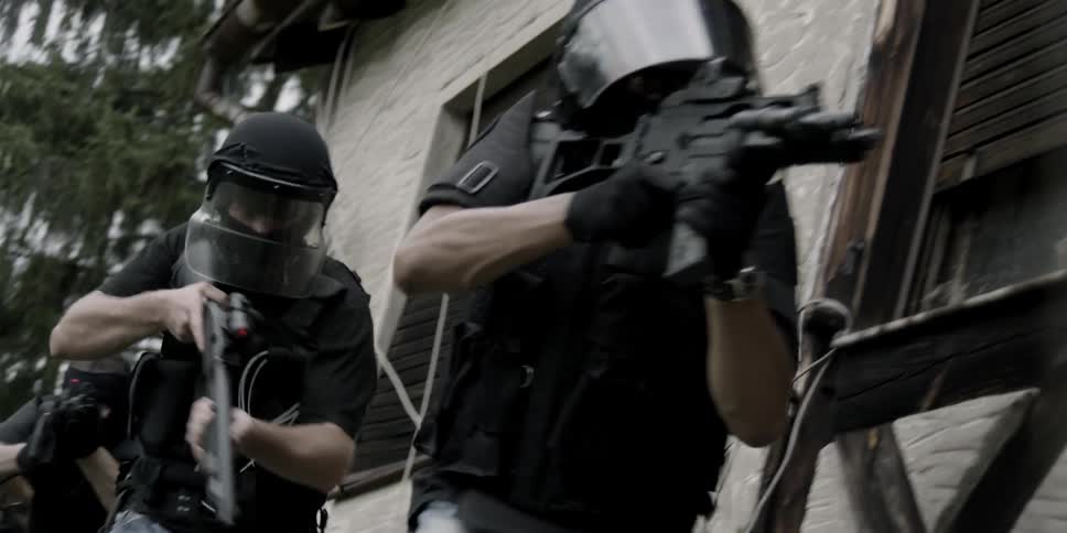 Armed police sneaking around the outside of a building