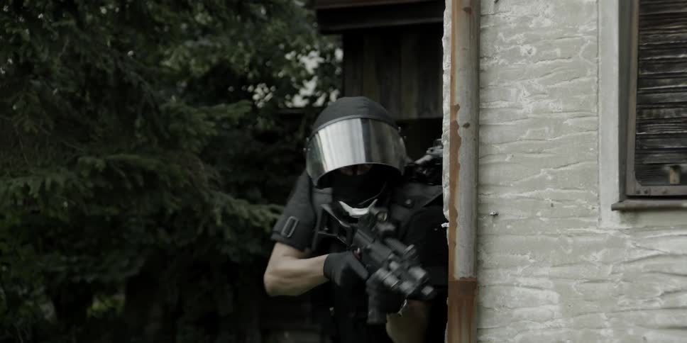A group of armed men rush past some trees and hide behind a building