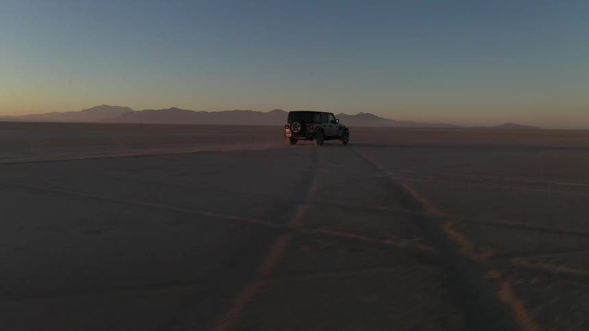A vehicle travels across a flatland in the desert in the evening