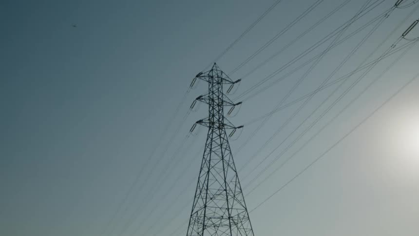 Many cables are connected to a utility tower as the sun shines in a hazy sky