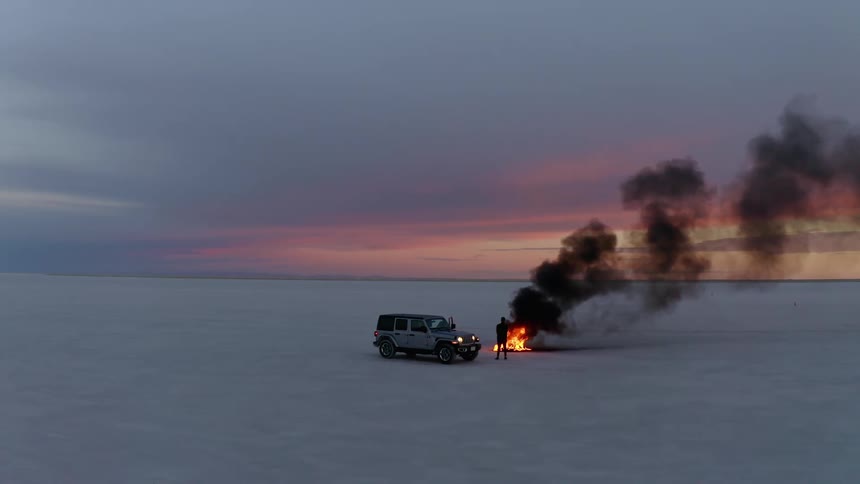 A young man is outside by his car and there is a fire in front of him