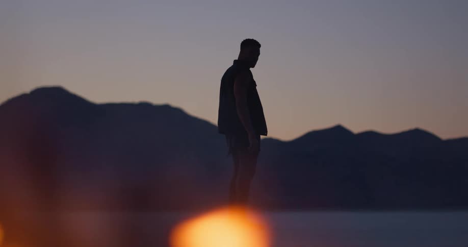 Silhouette of a man standing in the plains of a desert in front of a burning tire