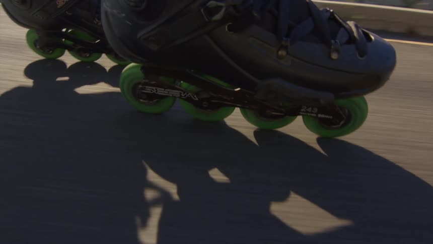 A person wearing roller blades with green wheels is rolling down a street
