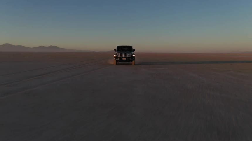 A jeep drives through a flat desert area as the camera orbits swiftly around it