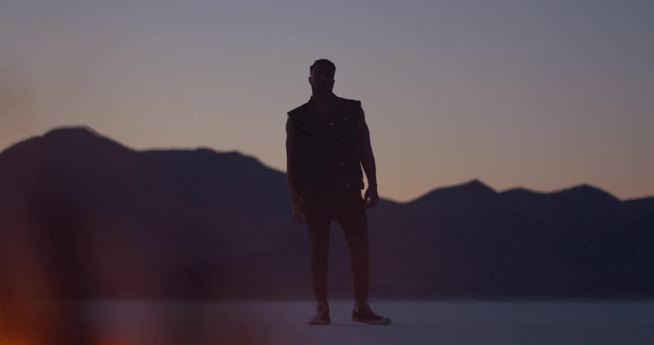 Silhouette of a man standing in the plains of a desert in front of a burning tire