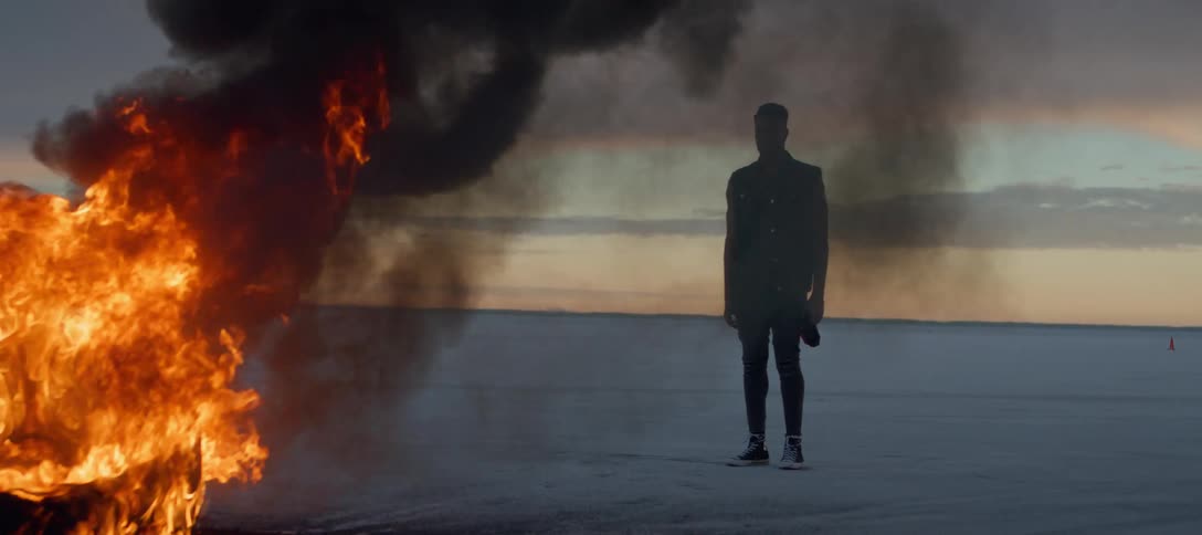A man standing in the desert watching a fire burn
