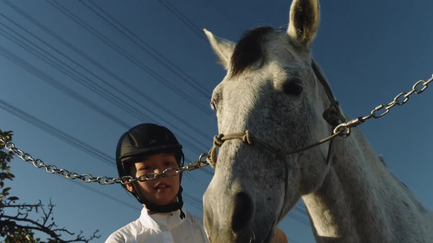 Female equestrian wearing a riding helmet grooms hair before kissing it