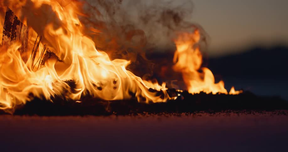 Dark smoke rises from fire with silhouetted mountains in the background