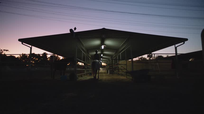 Person rides horse into open air barn under a red tinted sky