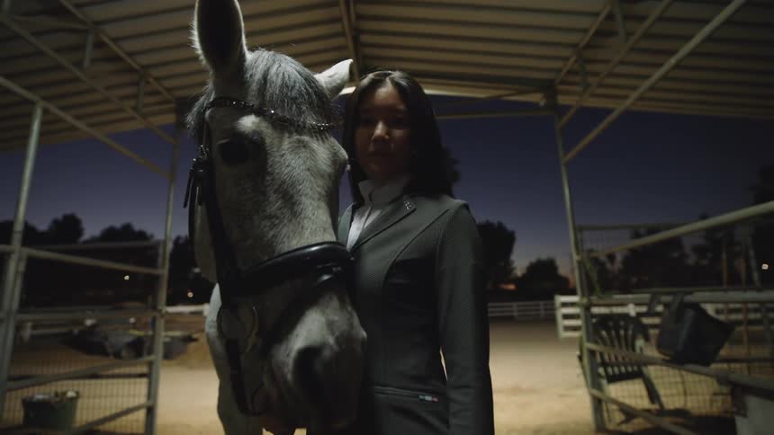 A woman stands and poses with a large horse that tries to touch the camera