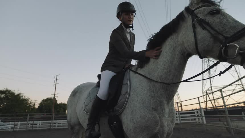 A female horse rider pets her horses mane while sitting on its back