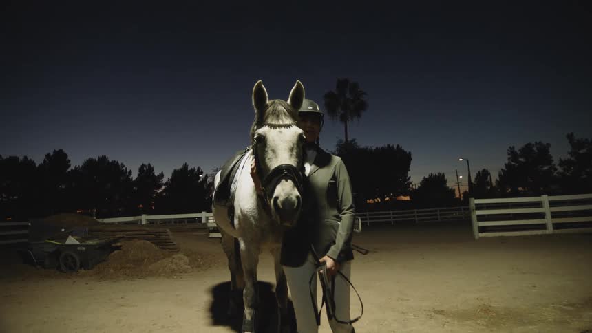 A girl stands in a pasture with her horse and pets it