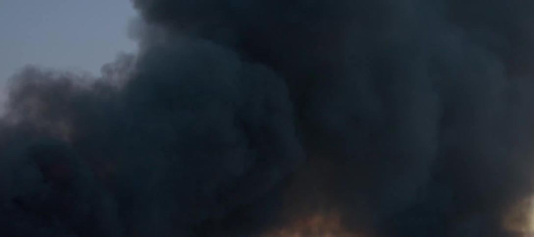 Thick black smoke rises from a blazing fire and covers the sky