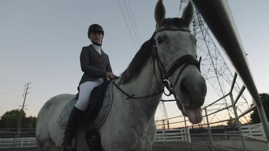 A young white woman is riding a horse outside in the middle of the day