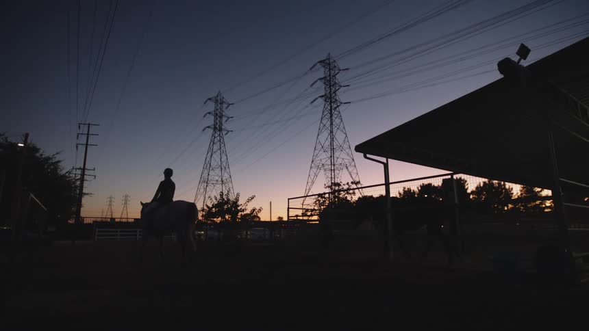 A girl rides a horse on a farm with electrical towers