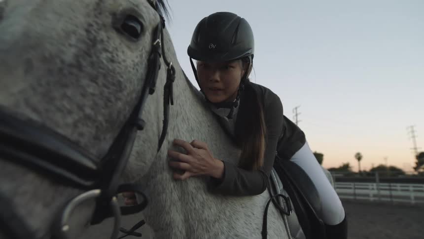 A girl wearing a helmet and sits on her horse scratches her horses neck