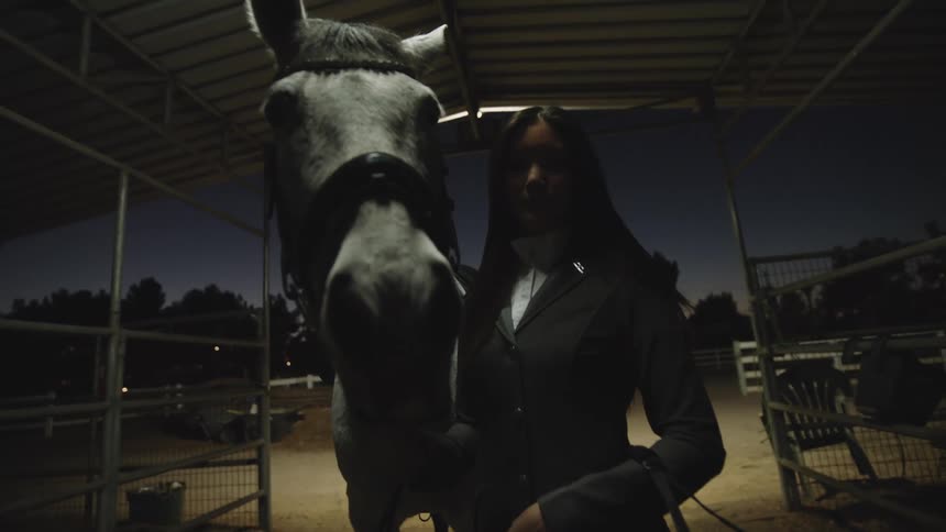 A woman is standing with her horse next to some stalls