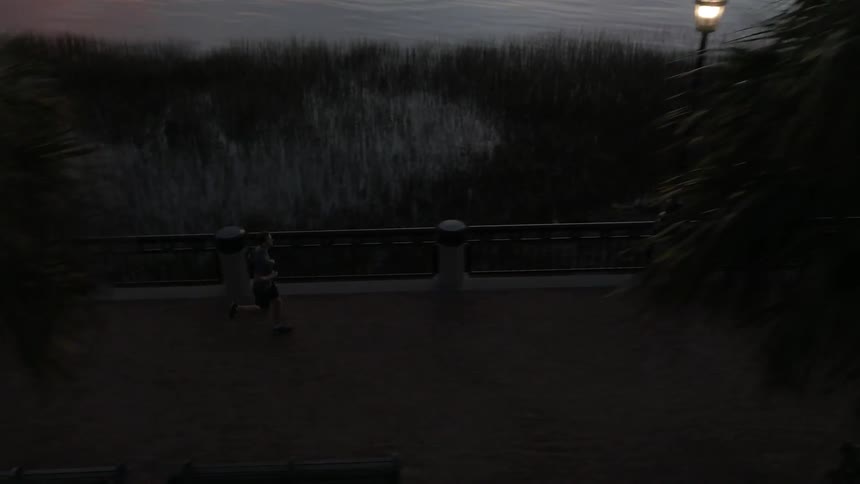 A man jogging on a path next to a shoreline as the sun sets