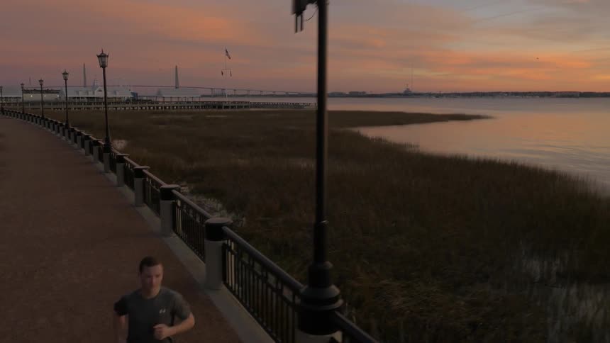 A man jogs on a boardwalk along a shoreline at dusk