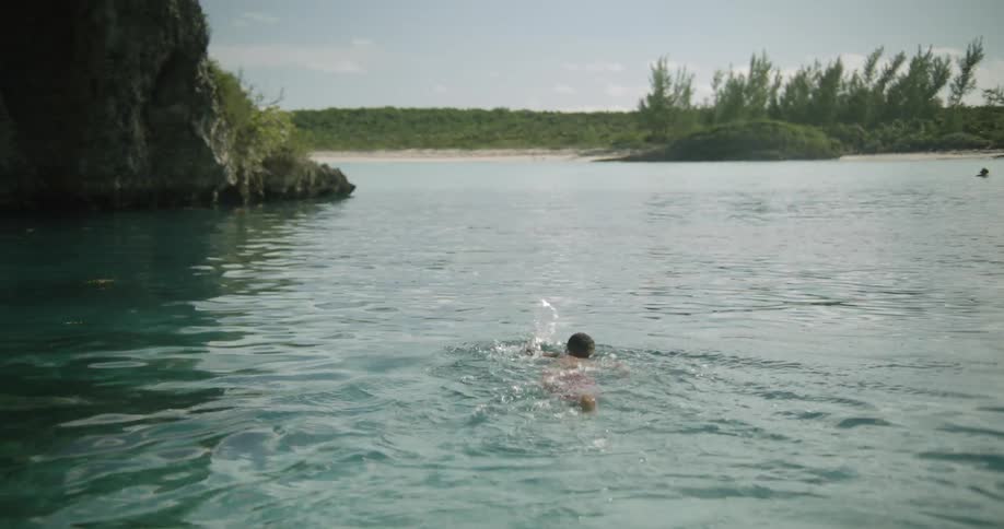 Male swimmer swims through water near base of cliff