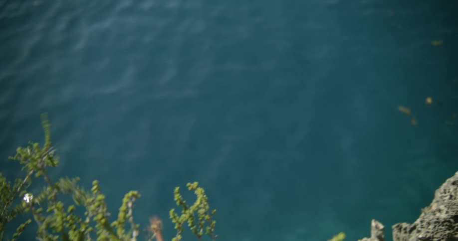 A boy jumps off a cliff into the ocean