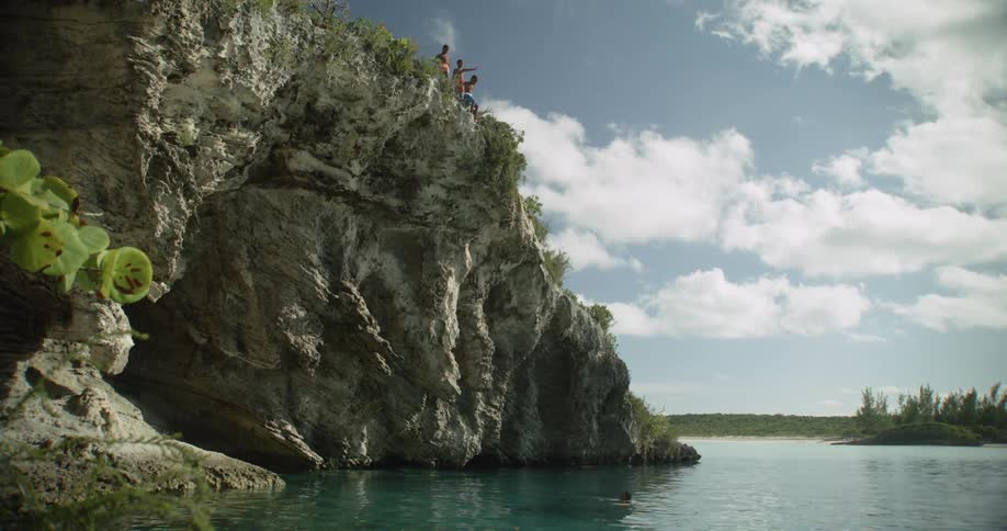 A group of young boys jump off a cliff into the sea