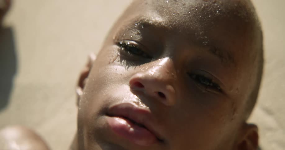 A boy lying on a sandy beach and smiling while an ocean wave washes over his body