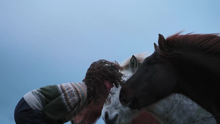 A younger white woman is outside and hanging out with some horses
