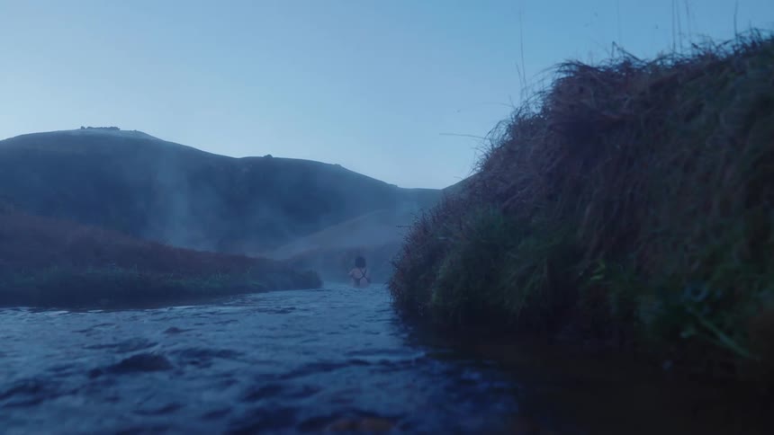 Woman wearing a swimsuit stands on a river in the countryside at morning