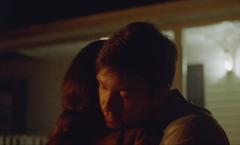 A man and woman hugging outside of a house at night