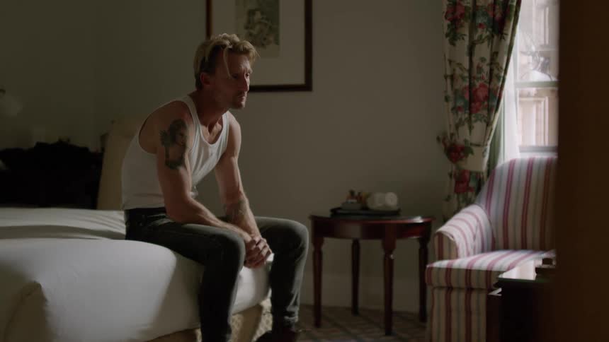 A man sits down at the end of his bed