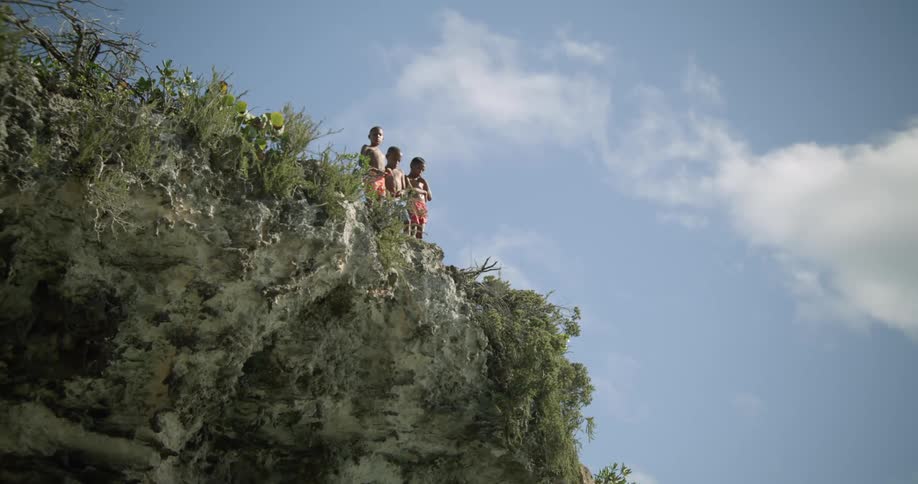 A group of young boys stand on the edge of a cliff and look down