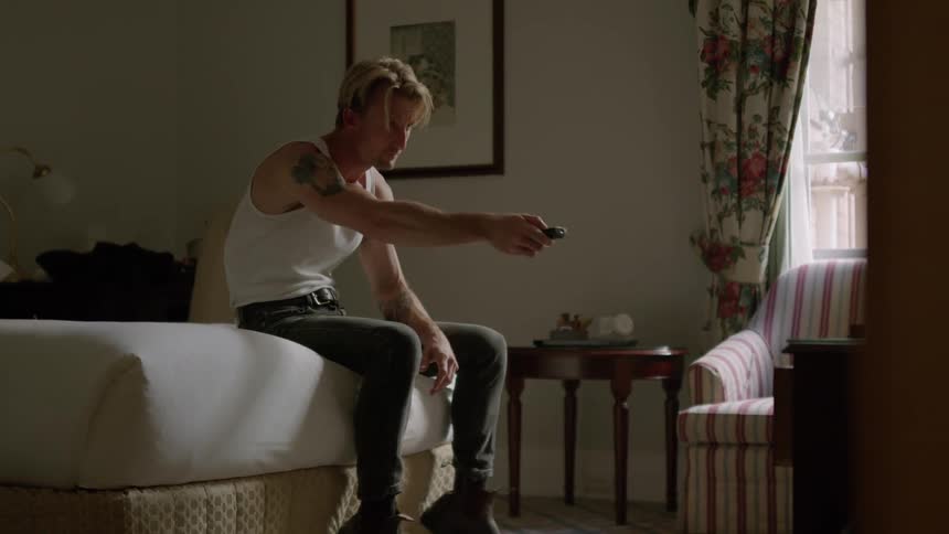 Bored tattooed man sitting on the bed change channels on the television with a remote control