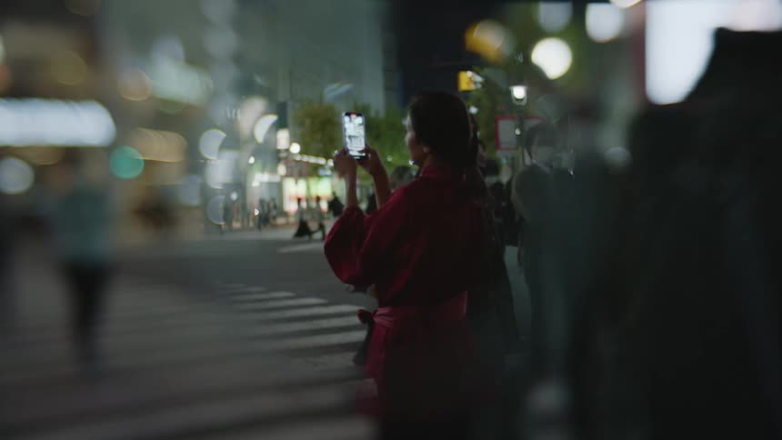 Woman in red dress takes photograph with smartphone in downtown area at night in the city
