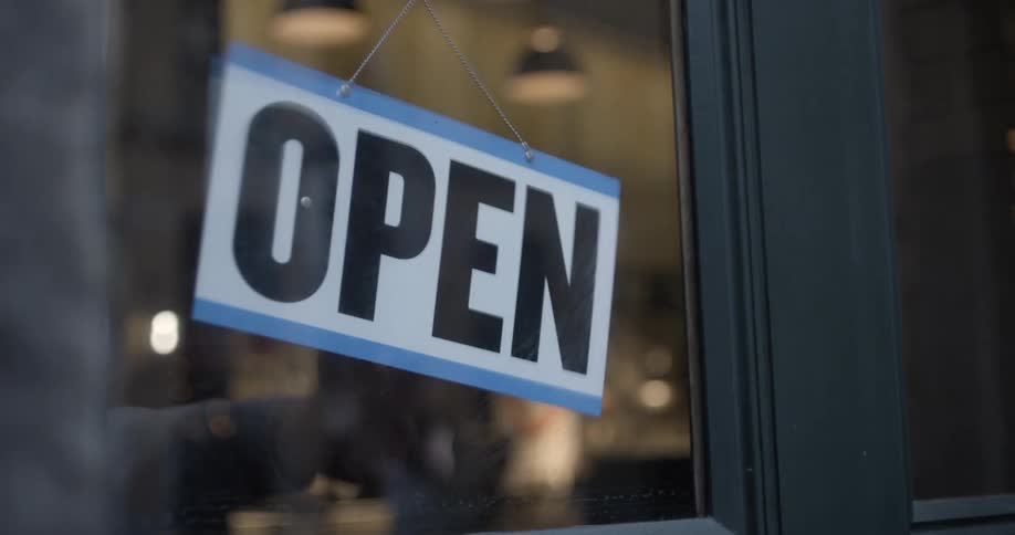 A man turns the sign to his business from closed to open