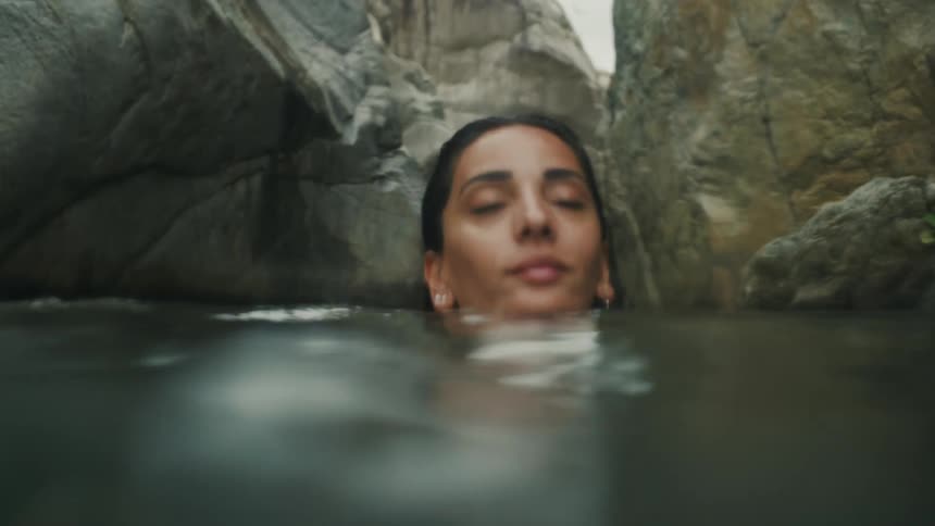 A woman swims through the waters on the floor of a ravine on a cloudy day