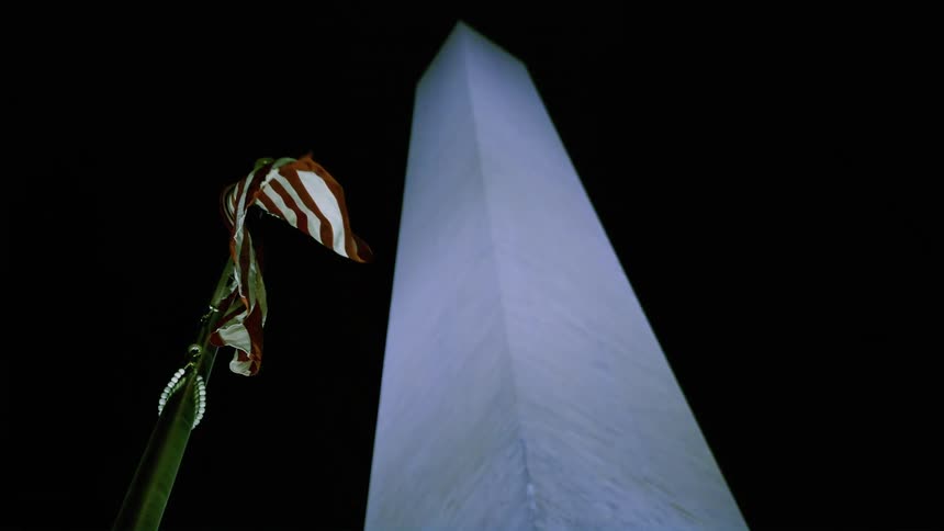 A flag is displayed near a tall skyscraper at night