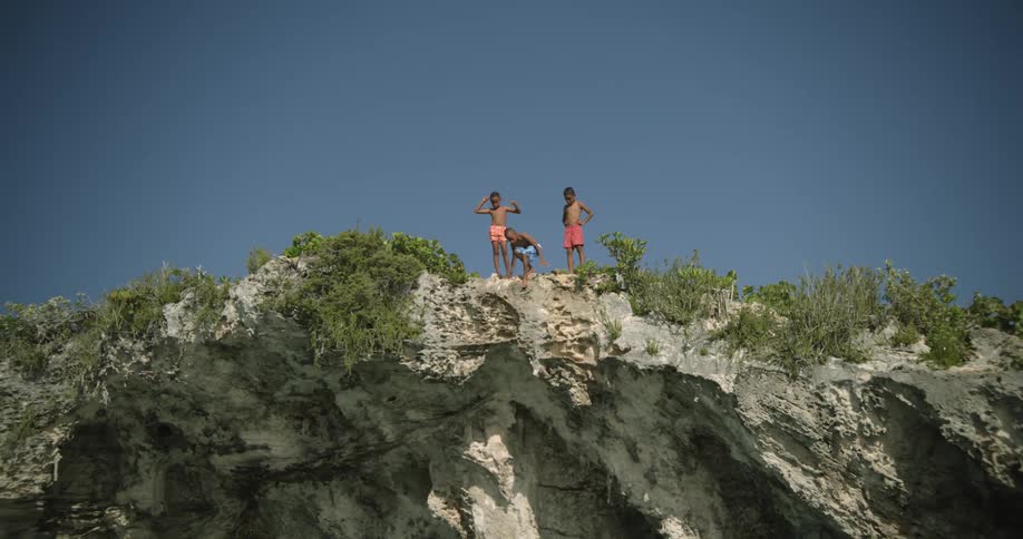 Young boy jumps into a lake from a tall cliff while friends watch
