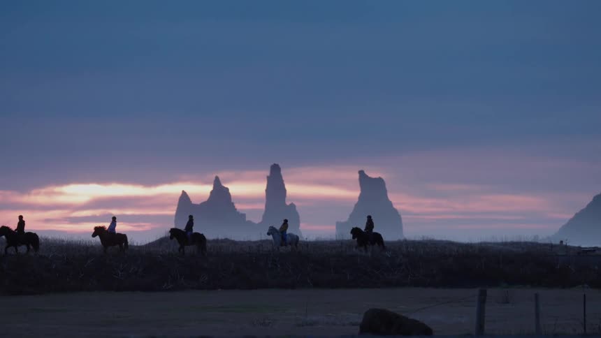Iceland - A group of people are horseback riding at dusk in Iceland