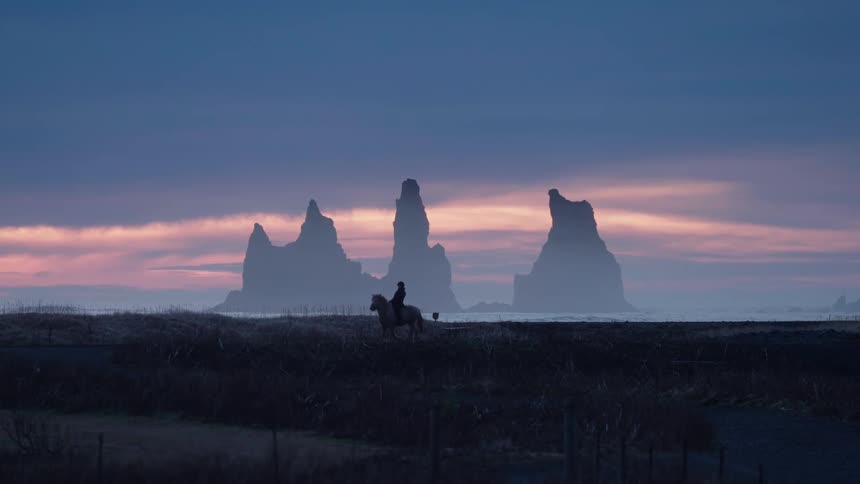 Iceland - Horse and rider trotting across a pasture in the country at sunrise in Iceland